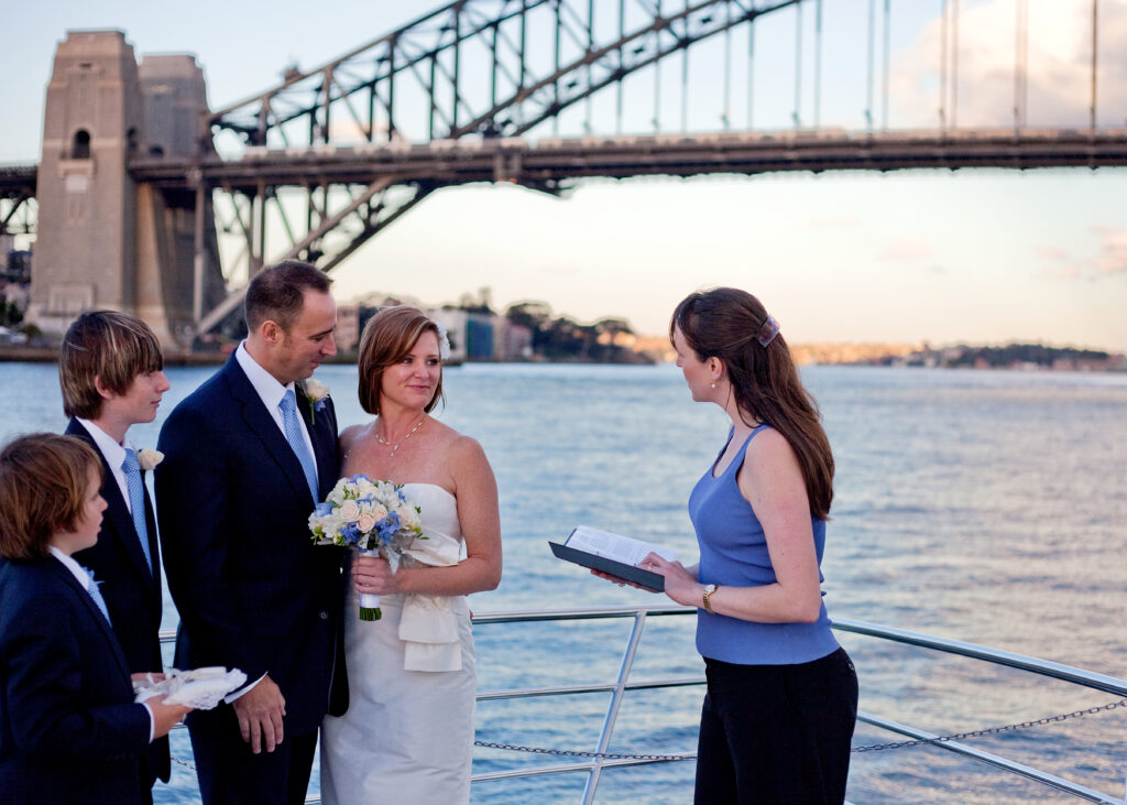 Couple getting married with two young boys standing to their left. Celebrant standing to right talking to couple. Water and Sydney Harbour Bridge in background.